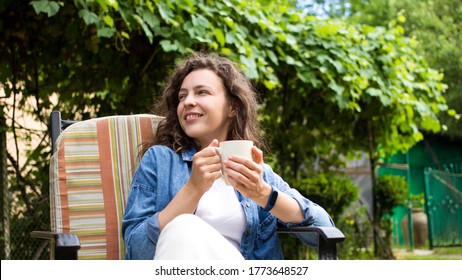 Portrait Of Dreamy Young Woman Enjoying Drinking Coffee In The Morning Sitting On Chair On Home Terrace On Green Garden Background.Happy Morning Routine,day Planning,enjoying Life,to Be In The Moment