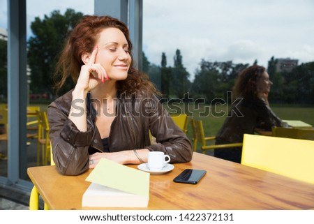 Portrait of dreamy young woman sitting at cafe table. Pretty lady closing her eyes when thinking about something pleasant. Fantasy concept 