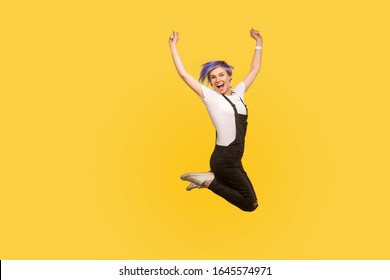 Porträt von ekstatischen, lebhaften, energischen hipster Mädchen mit violettem Haar in Overalls springen in Luft feiern Sieg, persönlicher Erfolg, freudig großen Verkauf. einzeln auf gelbem Hintergrund, Studioaufnahme