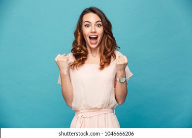 Portrait of ecstatic woman 20s wearing dress screaming and clenching fist like rejoicing victory or triumph isolated over blue background - Shutterstock ID 1046666206