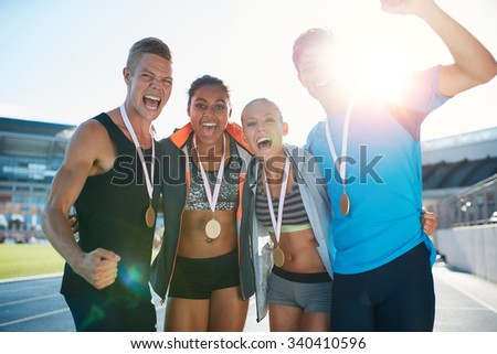 Portrait of ecstatic young runners with medals celebrating success in athletics stadium. Young men and women looking excited after winner a running race.