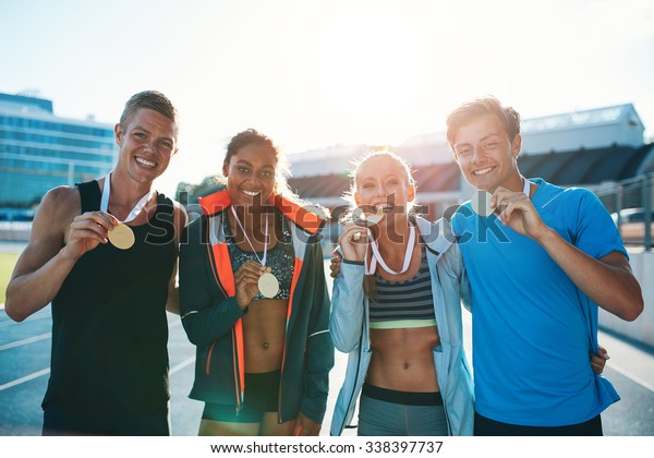 Portrait of ecstatic young runners\
showing medals. Young men and women looking excited after winner a\
running race. Team of multiracial athletes in\
stadium.