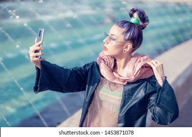 Portrait Of Edgy Girl With Crazy Look Taking Self-portraits (selfie). Urban Outdoor With Fountains In Background. Model Girl Wearing Stylish Sunglasses, Avant-garde Hairstyle And Make-up.