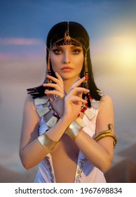 Portrait of Egypt Style woman. Sexy face girl goddess Queen Cleopatra in desert pyramids. Art ancient pharaoh costume white dress gold accessories. Egyptian makeup. Creative headband, snake bracelet