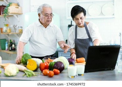 Portrait Of An Elderly Asian Couple Cooking In The Home Kitchen. They Have A Smiling Face, Happy, And Show Their Milk In Their Hands. Retirees Drink Milk To Make Bones Strong. Prevent Osteoporosis.