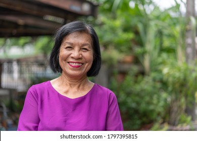 Portrait Of Elderly Asian Woman Smiling Standing In Front Of The House On A Green Tree Background.Healthy Old People Concept