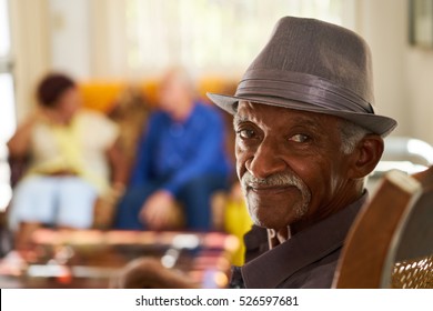 Portrait of elderly black man looking at camera in retirement home, with group of friends in background. Patients relaxing in hospice for seniors. 