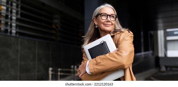 portrait of an elderly businesswoman with a laptop in glasses outside the office, strong and independent woman concept - Powered by Shutterstock