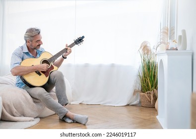 Portrait of elderly caucasian man musician as hobby. Senior male blogger teach guitar playing at living room. Handsome mature old man in casual clothes is smiling while playing guitar at home. - Powered by Shutterstock