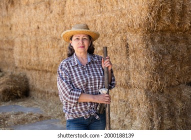 Portrait Of An Elderly Confident Woman Farmer, Standing Near The Haystacks, Holding A Pitchfork In Her Hand. Close-up ..portrait