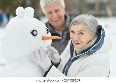 Portrait Of Elderly Couple Making Snowman And Shows Thumbs Up In Winter