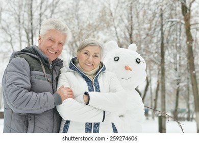 Portrait Of Elderly Couple Making Snowman And Shows Thumbs Up In Winter