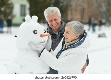 Portrait Of Elderly Couple Making Snowman And Shows Thumbs Up In Winter