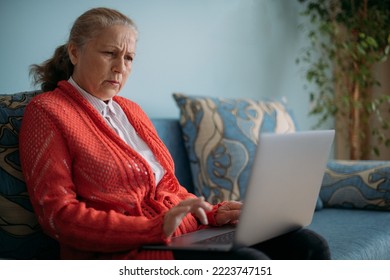Portrait of an elderly, dissatisfied retired woman at home on a laptop. An emotional, angry older woman looks at her laptop and frowns - Shutterstock ID 2223747151