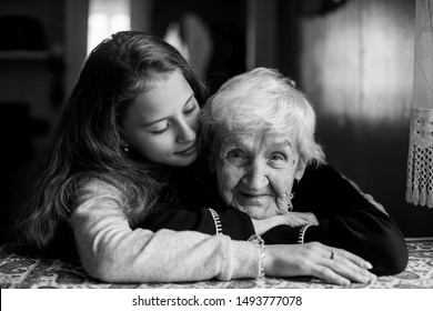 Portrait Of An Elderly Gray-haired Woman With Her Beloved Granddaughter. Black And White Photo.