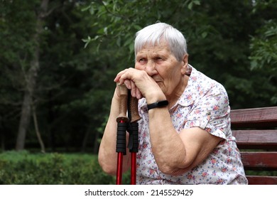 Portrait Of Elderly Gray-haired Woman Sitting With Walking Sticks On A Bench In A Park. Healthy Lifestyle In Old Age, Life In Retirement