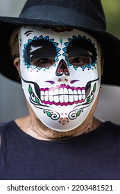 Portrait Of An Elderly Lady With A Catrina Mask And Hat, Celebrating Halloween And All Souls' Day, On The Street. Celebration, Costume, Party And Mask Concept.