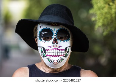 Portrait Of An Elderly Lady With A Catrina Mask And Hat, Celebrating Halloween And All Souls' Day, On The Street. Celebration, Costume, Party And Mask Concept.