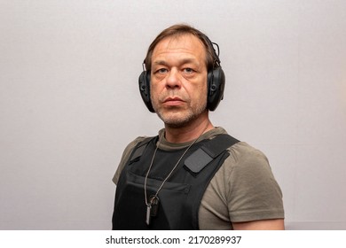 Portrait Of An Elderly Man 45-50 Years Old In A Bulletproof Vest And Tactical Headphones For Shooting On A Light Background.