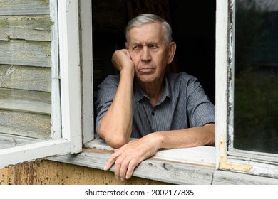 Portrait Of An Elderly Man Of 80 Years Old, Sad Looks From The Window Of An Old House. 