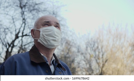 Portrait of elderly man with handmade mask on his face to protect himself from coronavirus pandemic. Close-up of man standing outdoors looking up at the sky. Concept of hope, faith, health and safety - Powered by Shutterstock