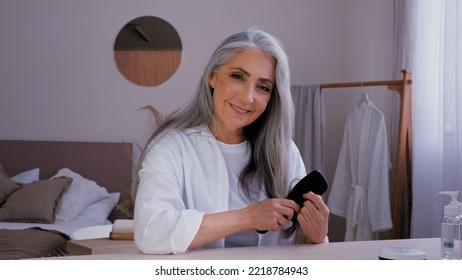 Portrait Elderly Mature Middle-aged Lady Old 50s Aged Caucasian Woman In Bathrobe Morning Beauty Routine Looking At Camera Combing Gray Long Shiny Hair With Comb Hairbrush Enjoy Healthy Hairstyle