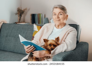 Portrait of Elderly retired senior woman with wrinkles smiling while embracing her Yorkshire terrier dog pet and relaxing while reading on sofa at home. Best friend. Enjoying retirement lifestyle. - Powered by Shutterstock