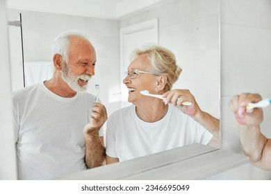 Portrait of an elderly senior couple cleaning brushing their teeth in front of mirror in bathroom. Dental hygiene, vitality, love and beauty concepts - Powered by Shutterstock