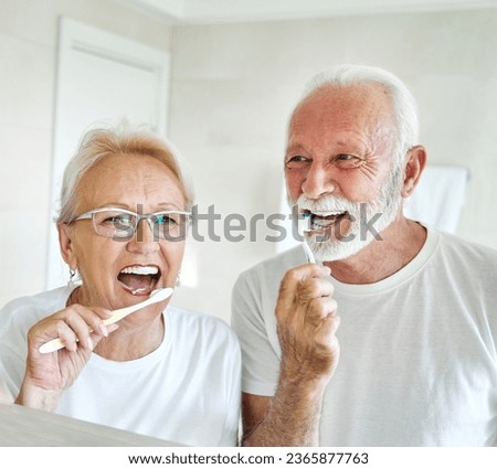 Portrait of an elderly senior couple cleaning brushing their teeth in front of mirror in bathroom. Dental hygiene, vitality, love and beauty concepts