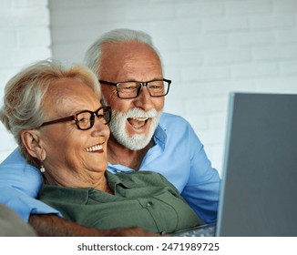 Portrait of an elderly senior happy couple using laptop at night, using modern technology having fun with glowing screen in dark office or at home, watching tv together at home. Shot of a mature  - Powered by Shutterstock