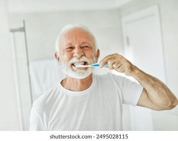 Portrait of an elderly senior man is cleaning brushing his teeth in front of mirror in bathroom. Dental hygiene, vitality and beauty concepts - Powered by Shutterstock