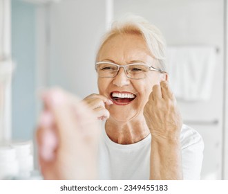 Portrait of an elderly senior woman is cleaning brushing his teeth using dental floss in front of mirror in bathroom. Dental hygiene, vitality and beauty concepts