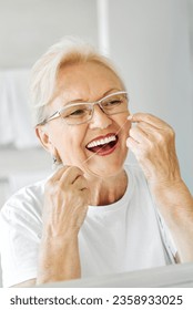 Portrait of an elderly senior woman is cleaning brushing his teeth using dental floss in front of mirror in bathroom. Dental hygiene, vitality and beauty concepts - Shutterstock ID 2358933025