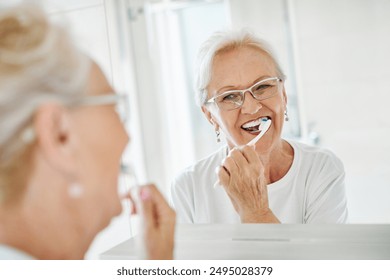 Portrait of an elderly senior woman is cleaning brushing his teeth in front of mirror in bathroom. Dental hygiene, vitality and beauty concepts - Powered by Shutterstock