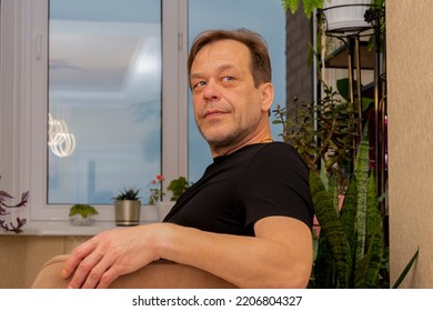 Portrait Of An Elderly Thoughtful Man Of 45-50 Years Old In A Black T-shirt In A Room Against The Background Of A Window.