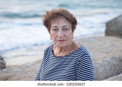 Portrait Of An Elderly Woman 80+ Relaxing On The Beach. Happy Granny, Pensioner With Light Make-up. Face With Wrinkles. Concept Of Pension, Good Quality Of Life, Health Insurance. Life Style. Sunset.