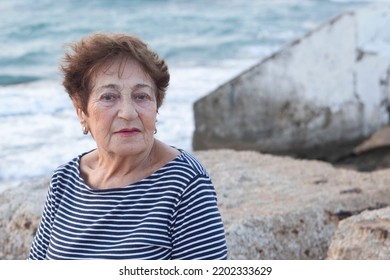 Portrait Of An Elderly Woman 80+ Relaxing On The Beach. Happy Granny, Pensioner With Light Make-up. Face With Wrinkles. Concept Of Pension, Good Quality Of Life, Health Insurance. Life Style. Sunset.