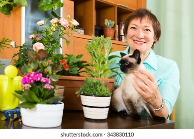 Portrait Of Elderly Woman With Decorative Plants And Cat At Home