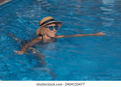 Portrait of an elderly woman in a hat and blue sunglasses swims in the pool.  - Powered by Shutterstock