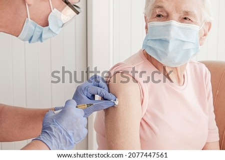 Portrait of elderly woman at the hospital being vaccinated by a female nurse. Senior lady wearing face mask getting an immunization shot. Close up, copy space, background.