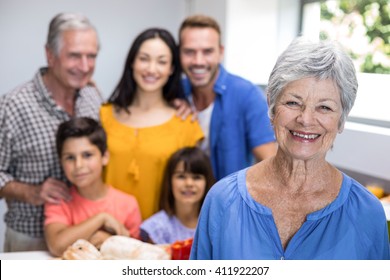 Portrait Of Elderly Woman In The Kitchen And Other Family Member Standing In Background