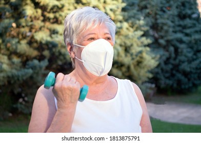 Portrait Of An Elderly Woman Protected With A Mask Exercising While Lifting Weights Outdoors.