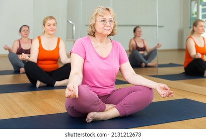 Portrait of elderly woman sitting in lotus position practicing meditation at group yoga class - Powered by Shutterstock