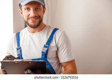 Portrait Of Electrical Technician In Uniform Smiling At Camera, Writing The Data Collected On A Residential Electric Panel