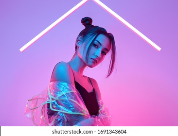 Portrait of elegant beautiful Asian woman in a fashionable raincoat around colourful bright neon uv lights posing in studio