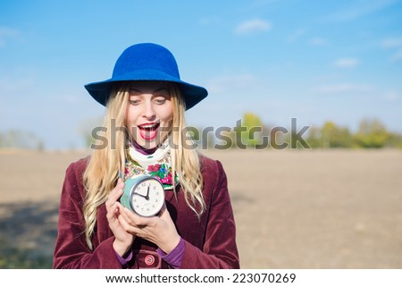 portrait of elegant beautiful blond young lady having fun holding retro alarm clock and happy smiling on sunny autumn outdoors copy space background