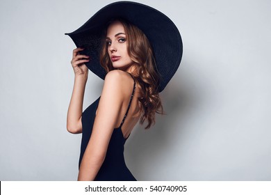Portrait of elegant beautiful woman in a black dress and wide hat isolated on white background in studio