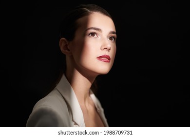 Portrait Of An Elegant Brunette Woman With Evening Makeup Standing In A Beam Of Light On A Black Background. Makeup And Cosmetics.