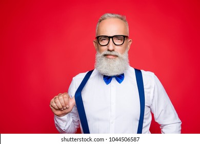 Portrait of elegant, confident macho, old barber, stylist draw off suspender with thumb finger, looking at camera with simper, isolated on red background - Shutterstock ID 1044506587
