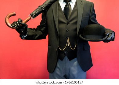 Portrait Of Elegant Man In Dark Suit And Leather Gloves Holding A Bowler Hat And Umbrella. Concept Of Classic British Gentleman Stereotype. Retro Style And Vintage Fashion.